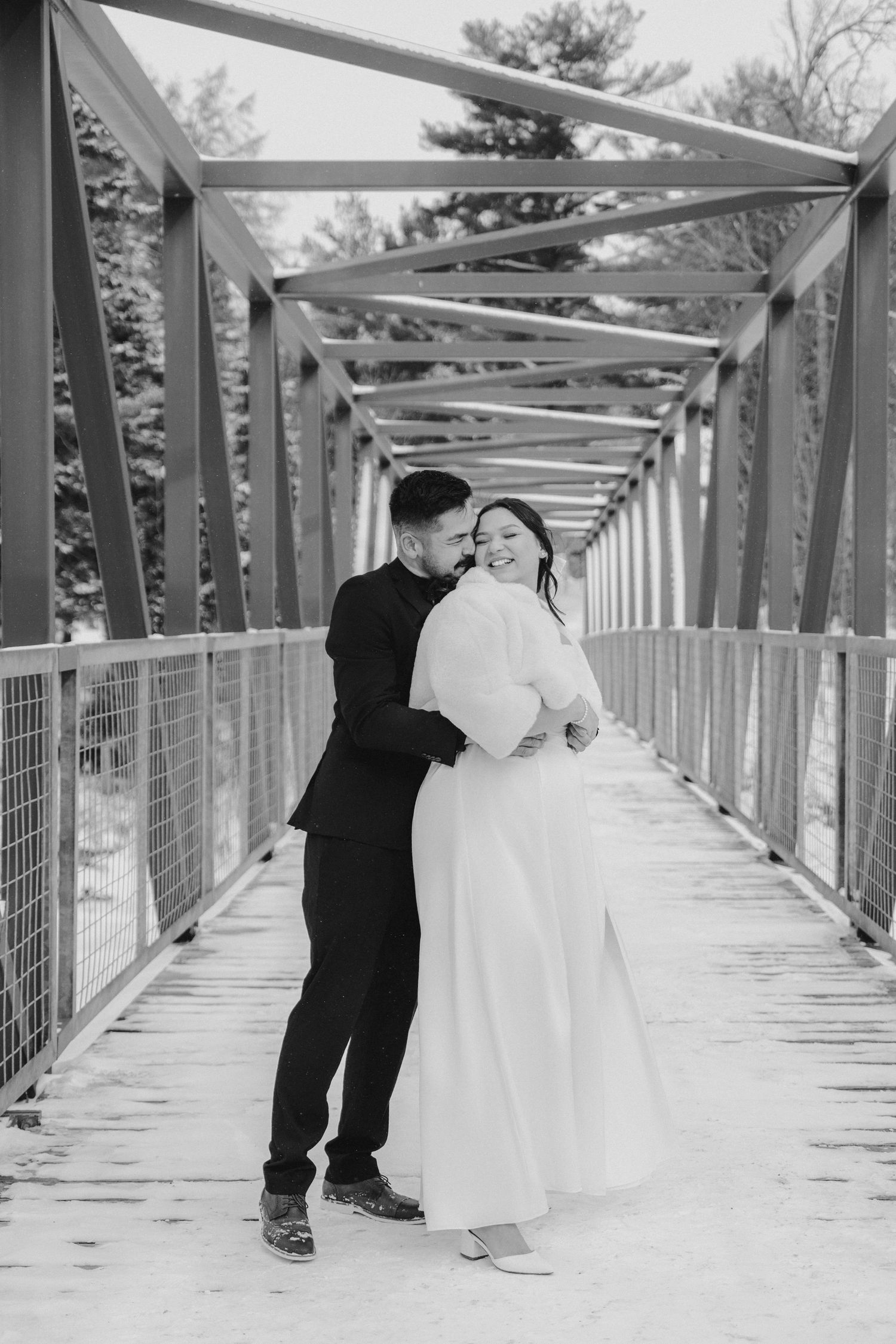 A couple walks hand in hand down a tree-lined path in black and white, with the bride wearing a flowing white dress.
