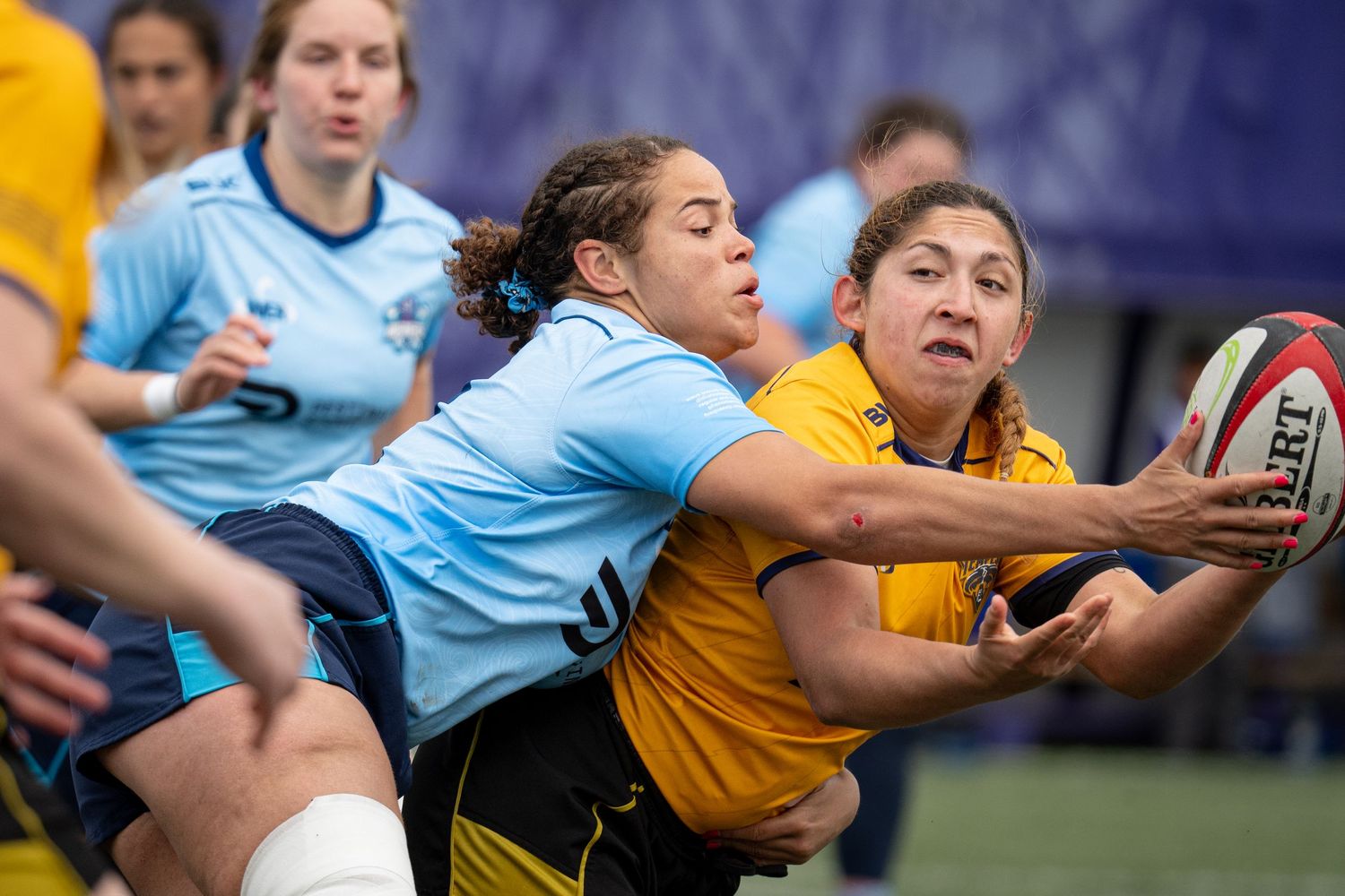 A Chicago Tempest rugby player attempts to pass the ball backwards to a teammate while an opponent blocks the ball