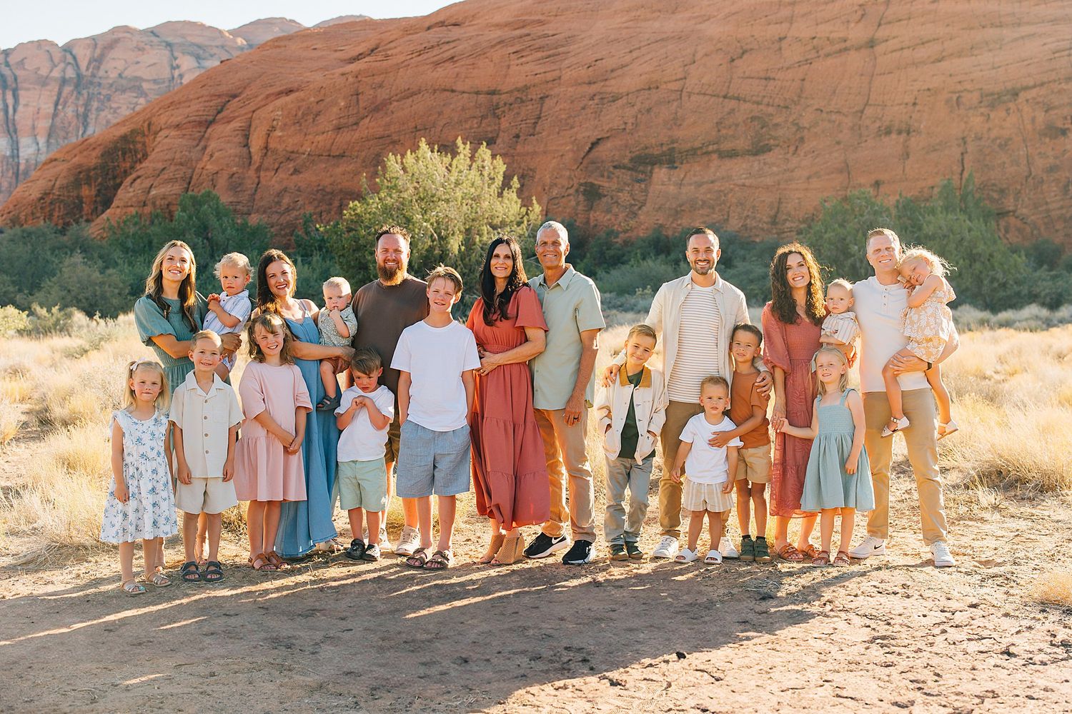 Extended family group poses together against backdrop of red rock formations in desert setting.