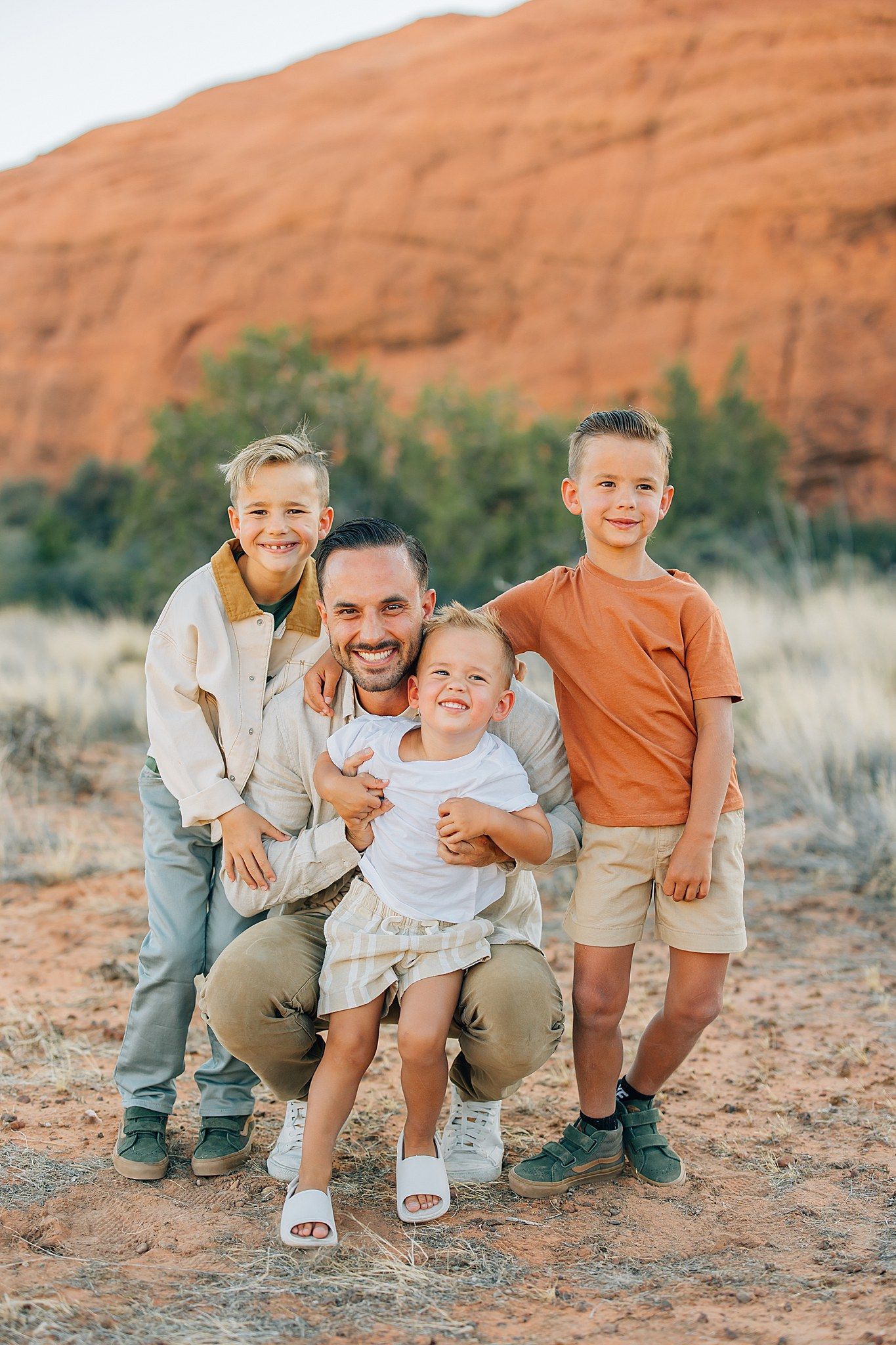 Family portrait taken outdoors against red rock formations in a desert landscape with brush and greenery.