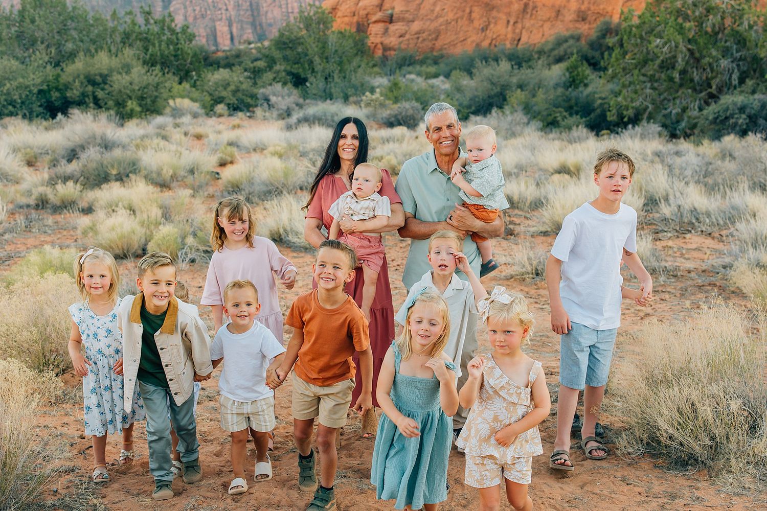Group portrait of people gathered outdoors with desert brush and red rock formations in the background.