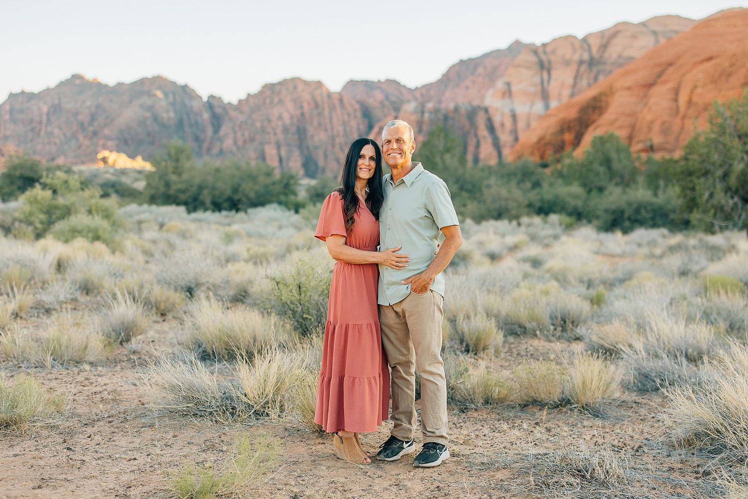A couple poses together in front of red rock cliffs at Snow Canyon State Park in Utah during sunset.