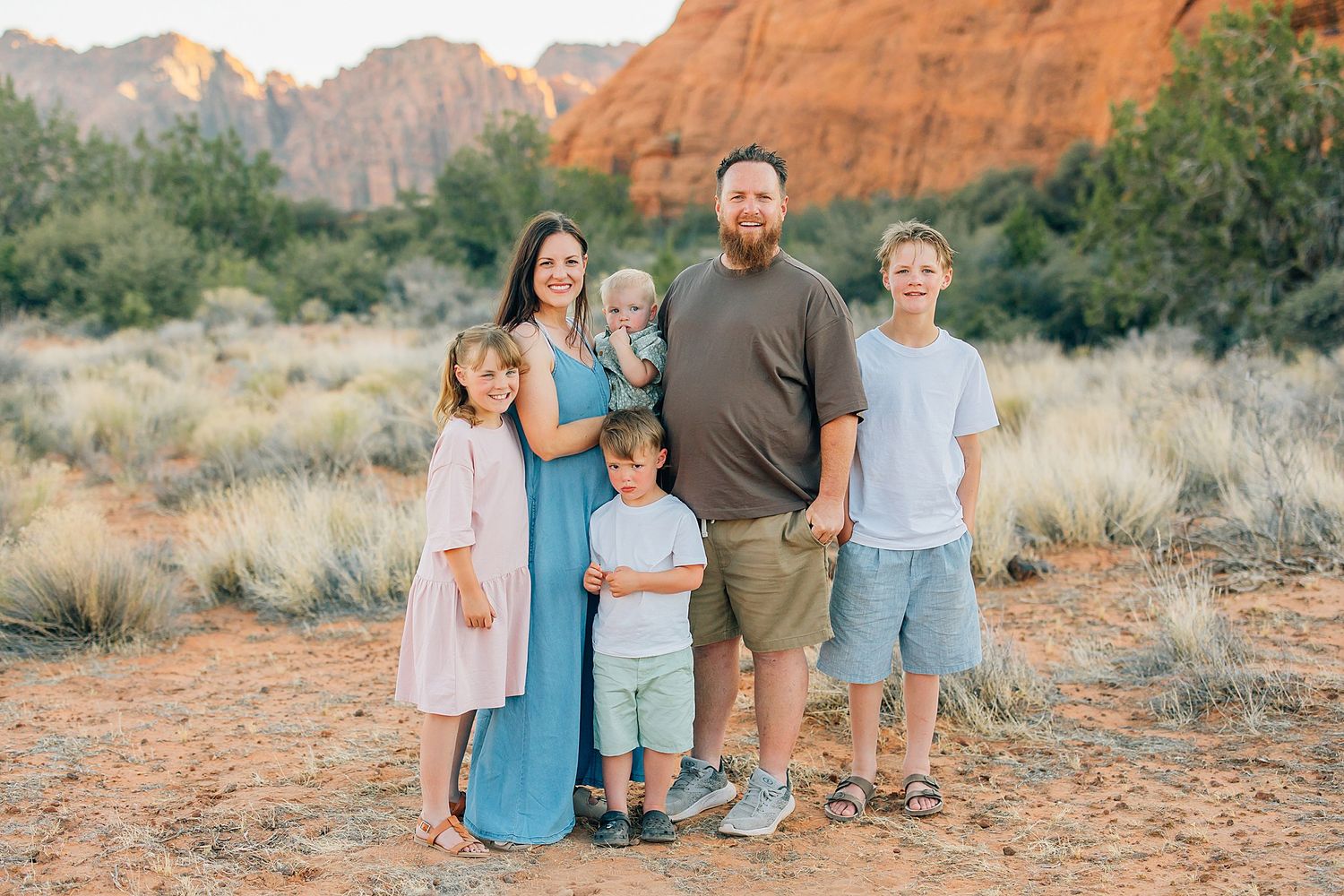 A family wearing coordinated blue and teal outfits poses together against red rock formations in a desert landscape.
