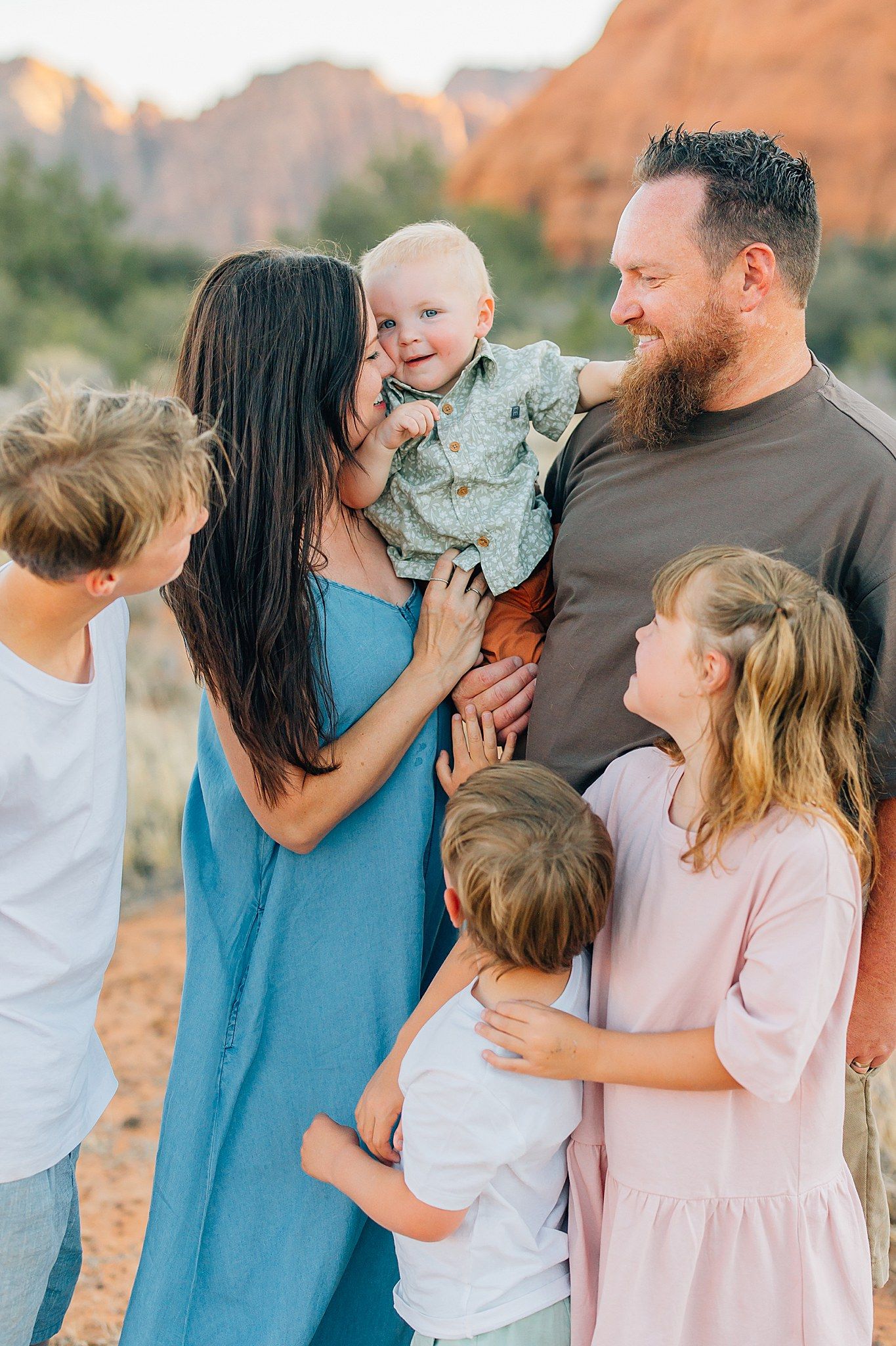 Family members share joyful moments together against a backdrop of desert rock formations at sunset.