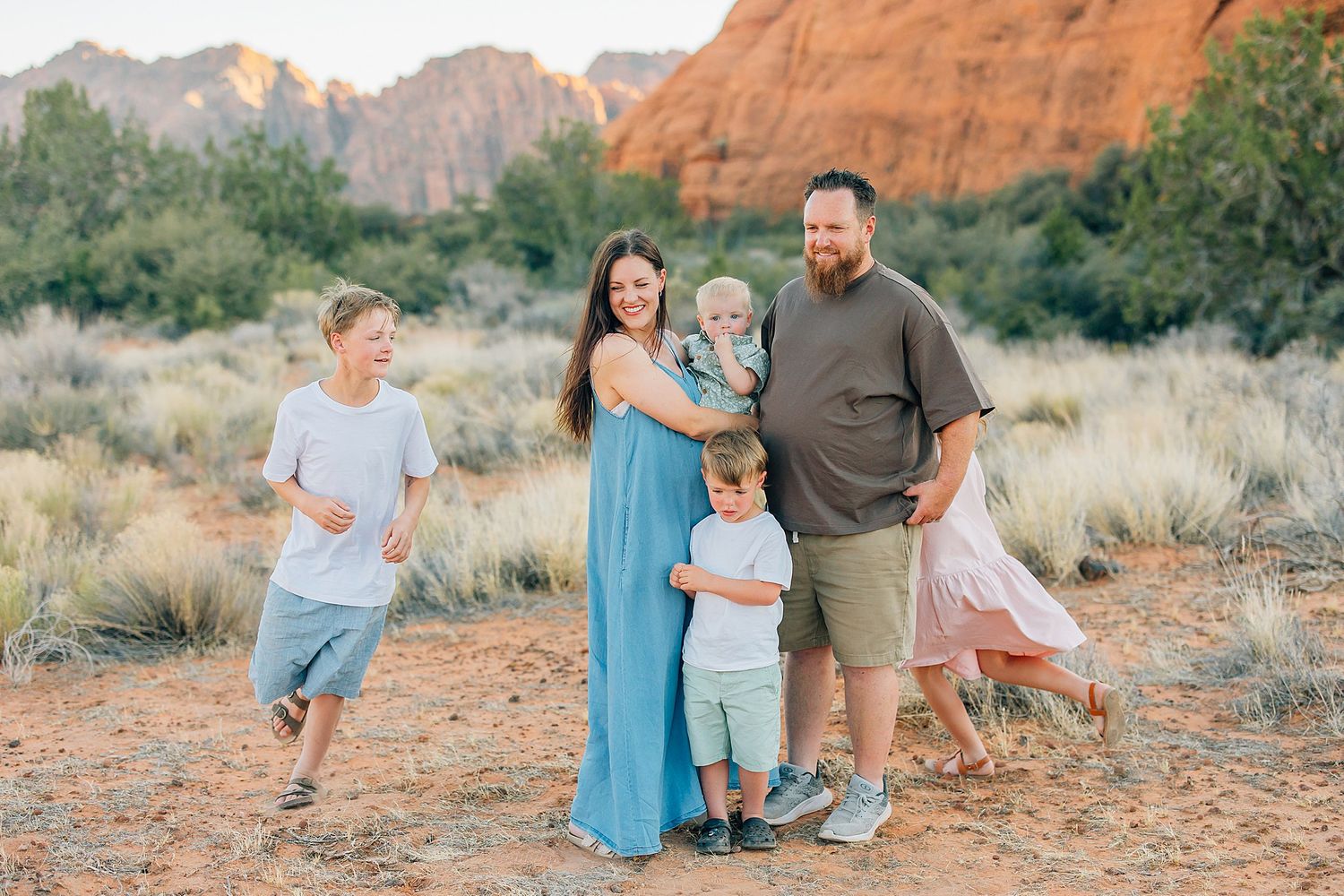 A group poses against stunning red rock formations in a desert setting during golden hour.