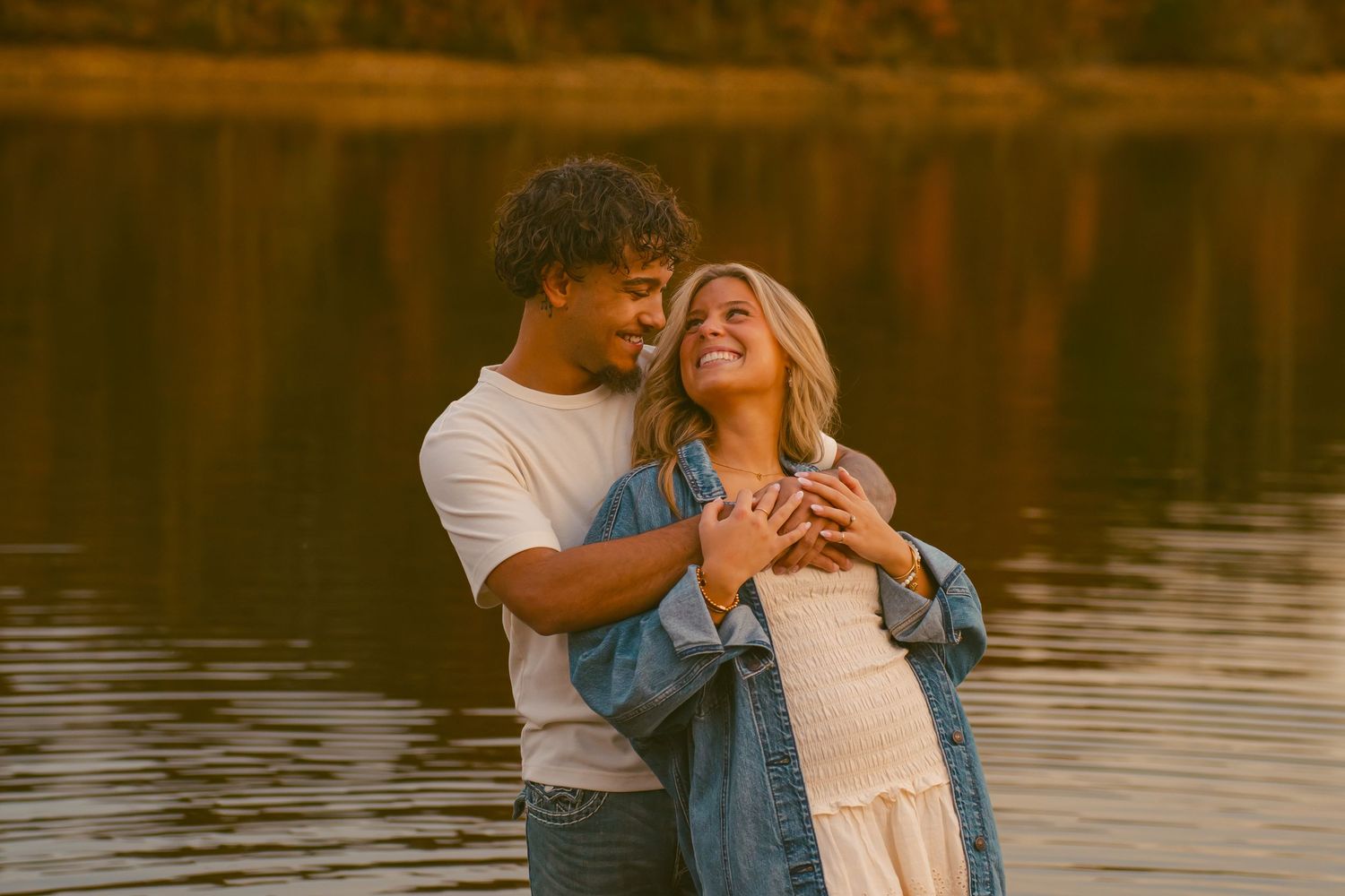 Romantic couple embraces during golden hour by a serene lake, creating a dreamy silhouette against the water.