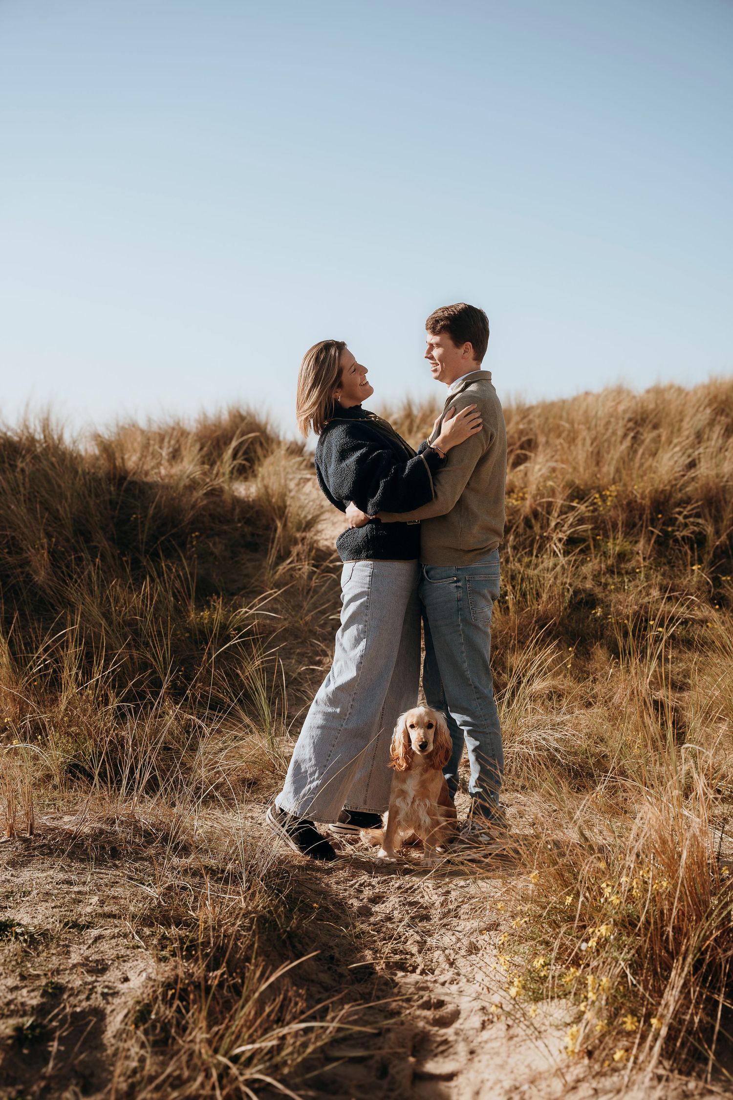 A black and white photograph capturing a tender family moment in a field of tall grass.
