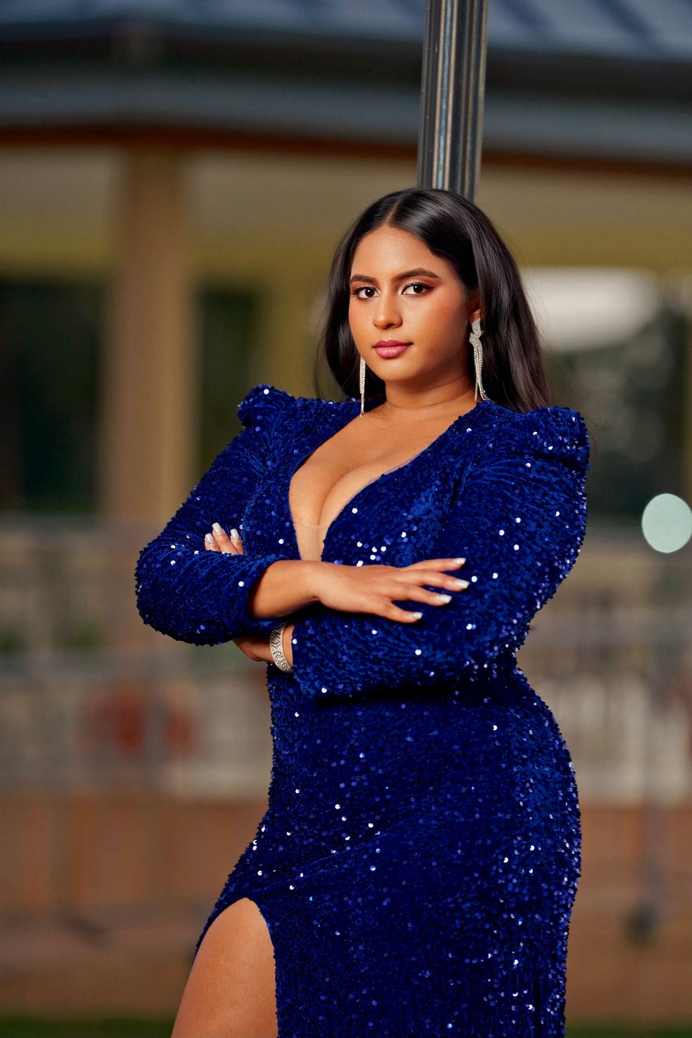 Woman in a sparkling royal blue evening gown with dramatic puff sleeves poses elegantly against a blurred background.