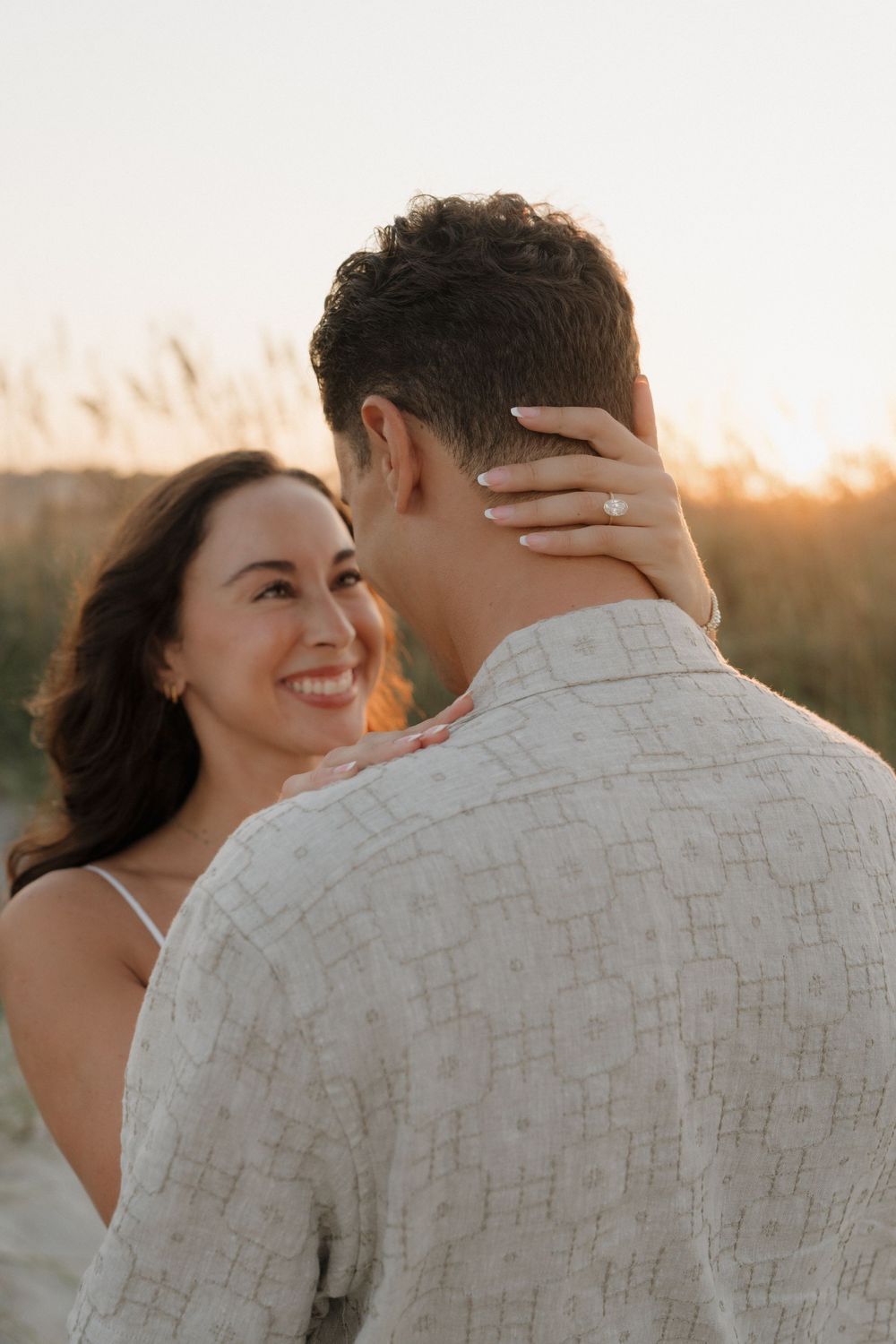 Romantic couple embraces during golden hour sunset photoshoot in a natural outdoor setting.