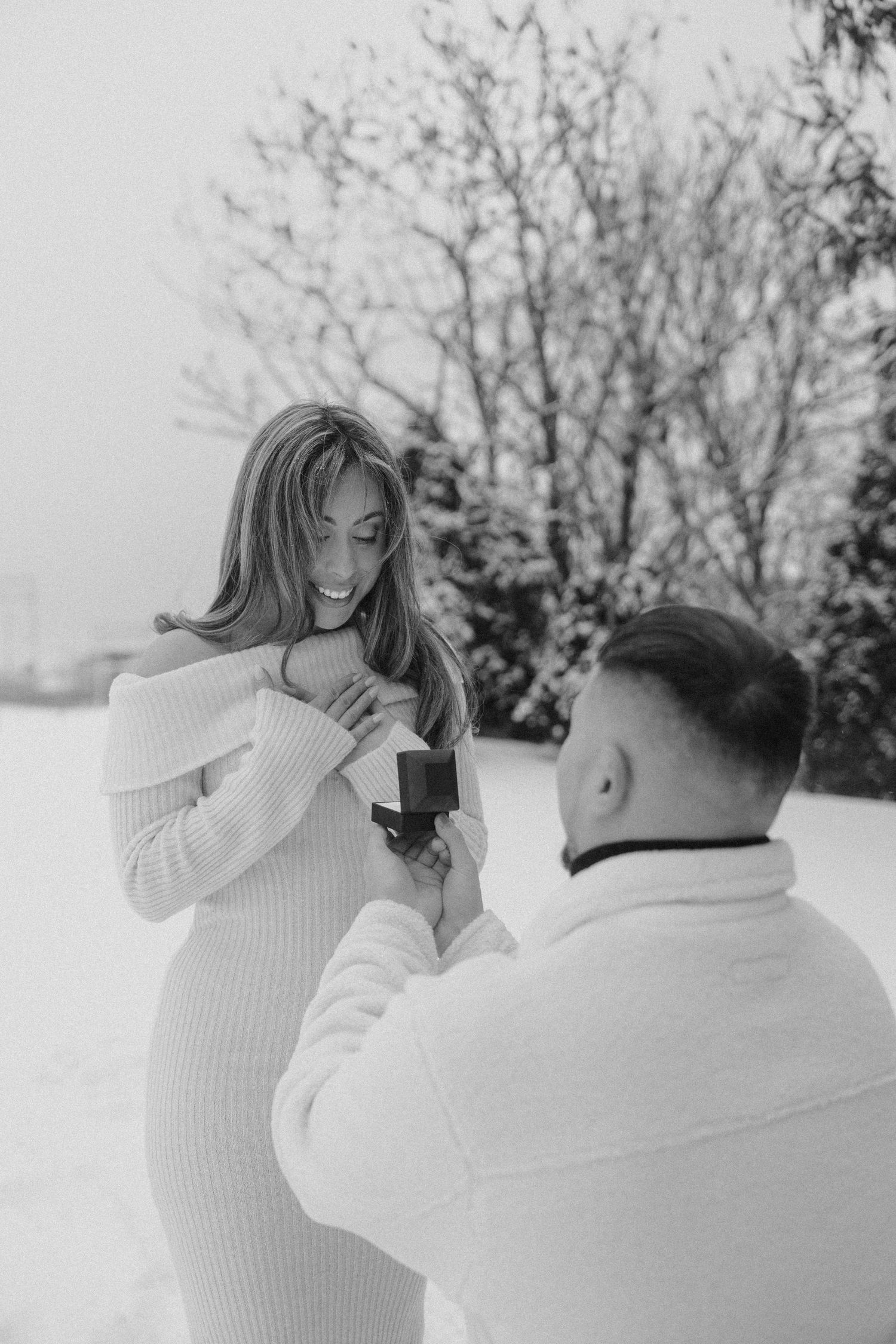 A couple in white sweaters shares candid moments during a winter photo session in the snow.