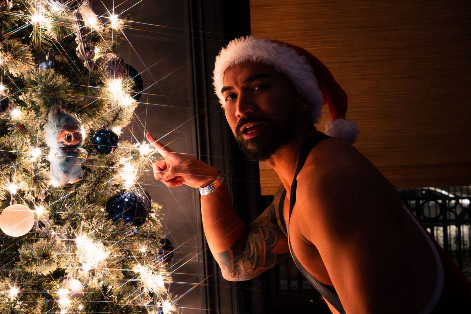 A person at a holiday-themed party in a Santa hat leans towards the Christmas tree with a finger outstretched