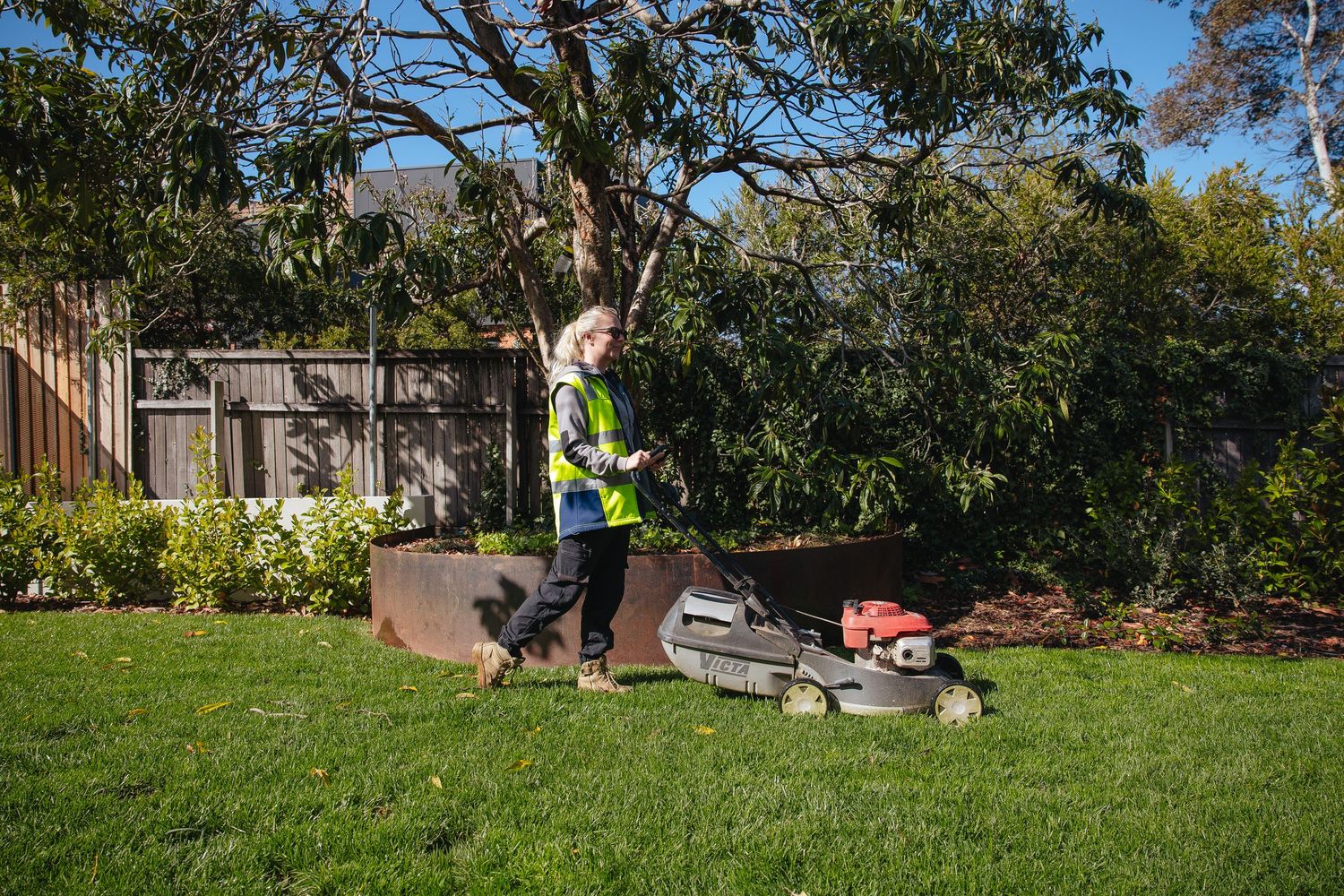 A panoramic view of a landscaping project showing multiple workers clearing and maintaining a green residential yard.