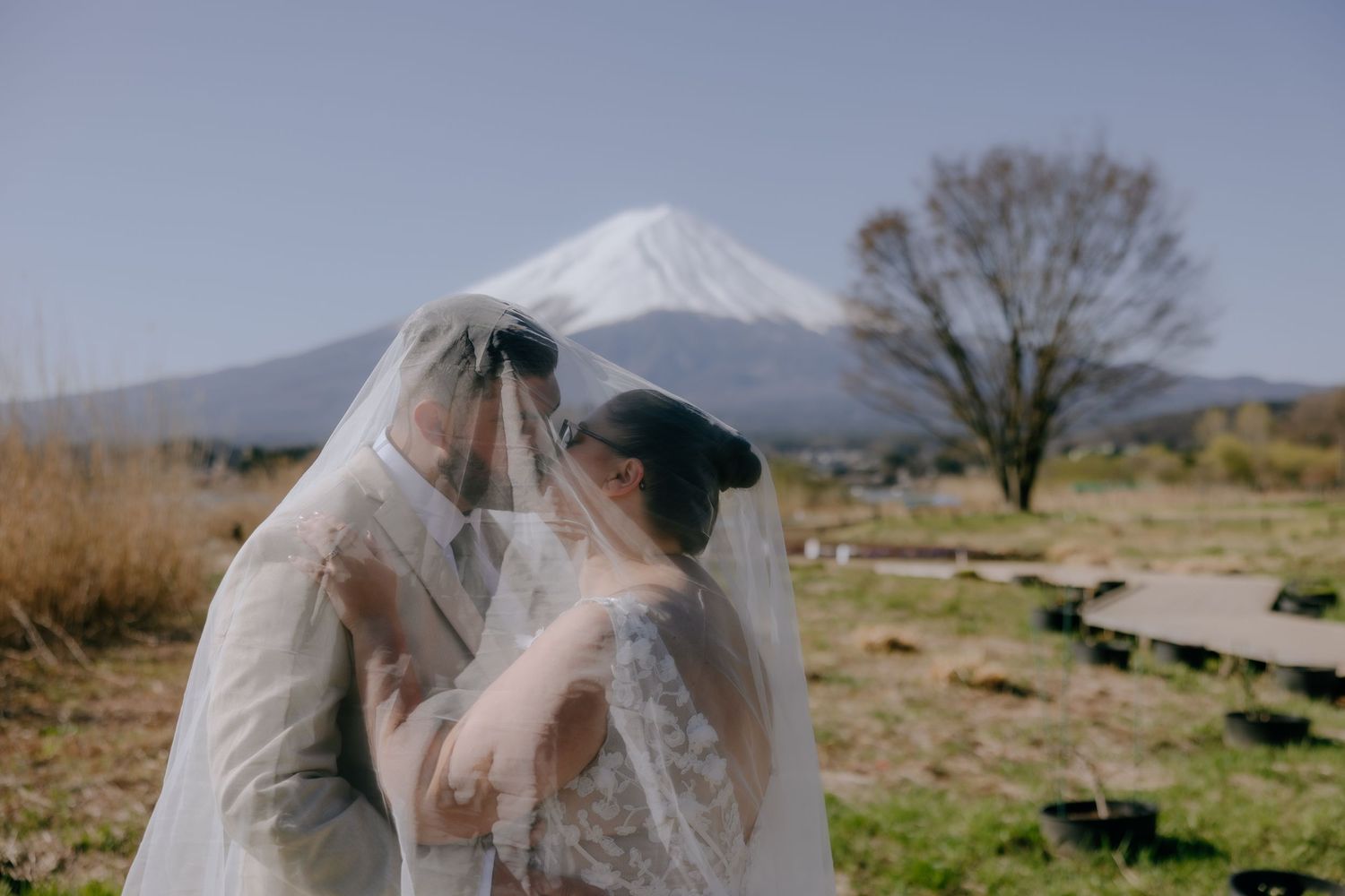 A romantic wedding moment captured with Mount Fuji rising majestically in the background on a clear day.