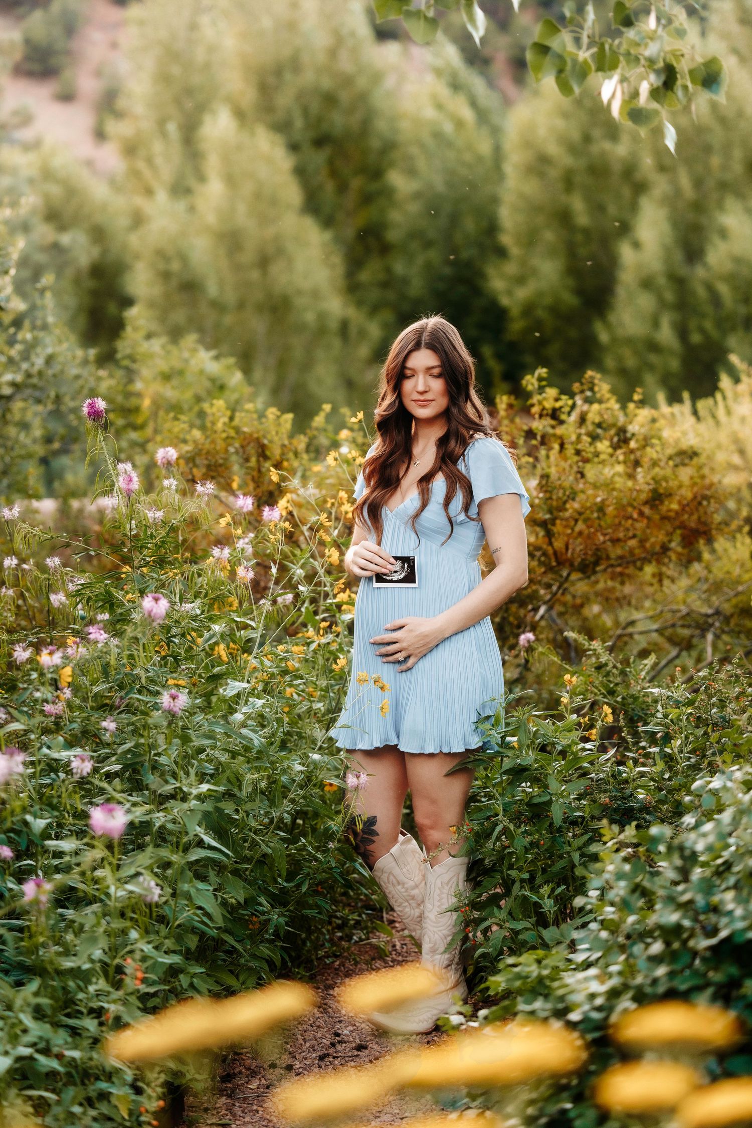Pregnant woman in flowing red gown standing on cliff edge with dramatic canyon landscape.