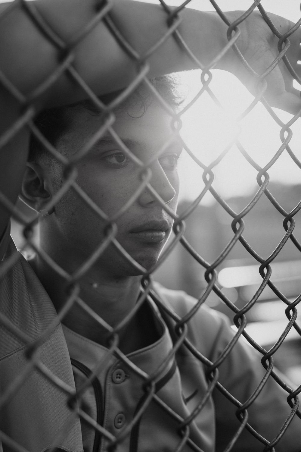 Artistic black and white close-up shot through chain link fence showing blurred silhouette and bokeh light effects.