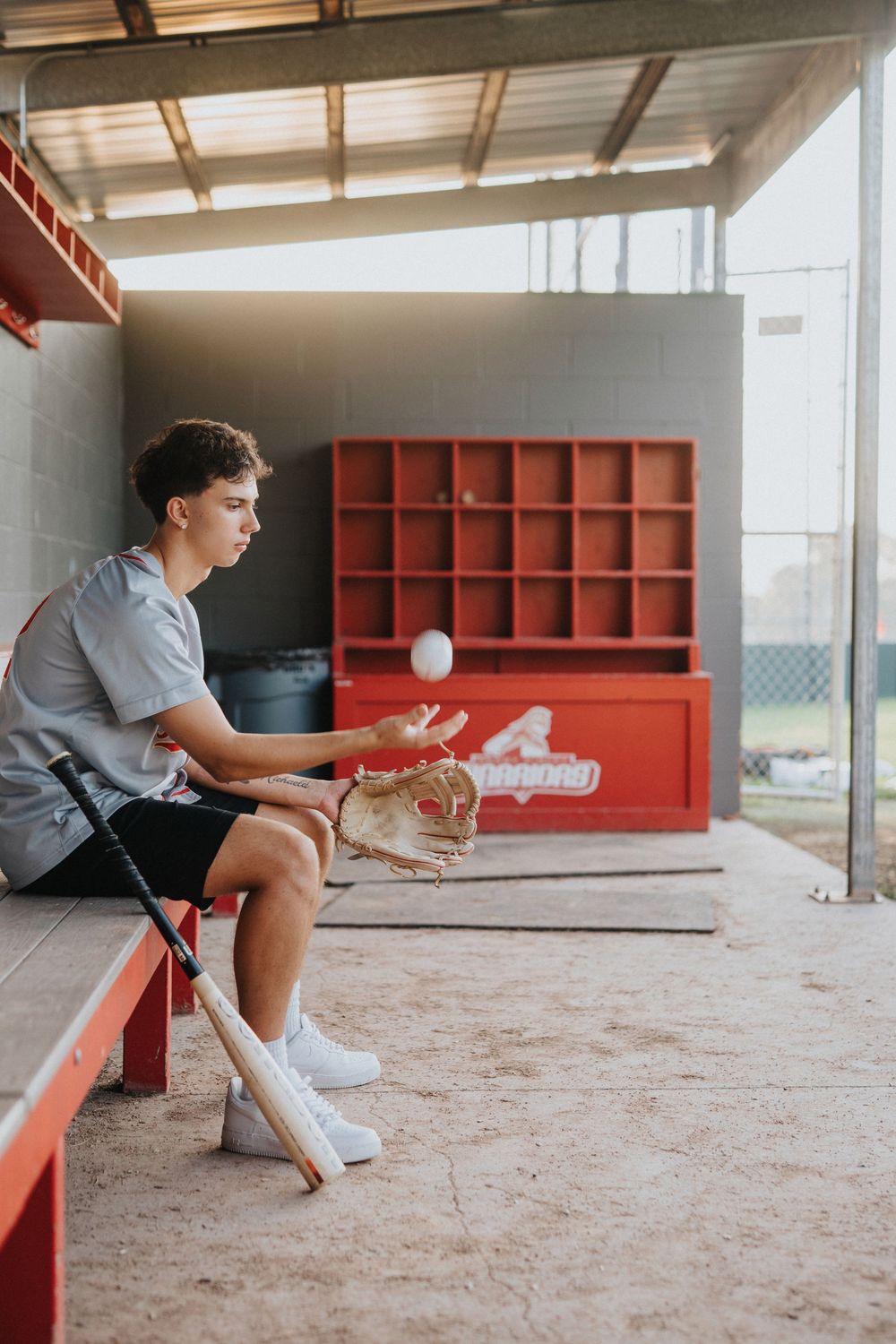 A baseball player sits in the dugout preparing equipment before a game.