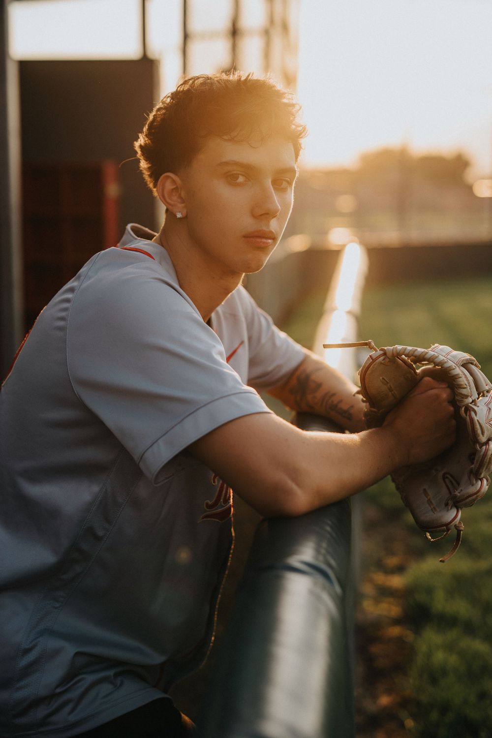 Baseball player in light blue uniform practices catching drills during golden hour sunset.
