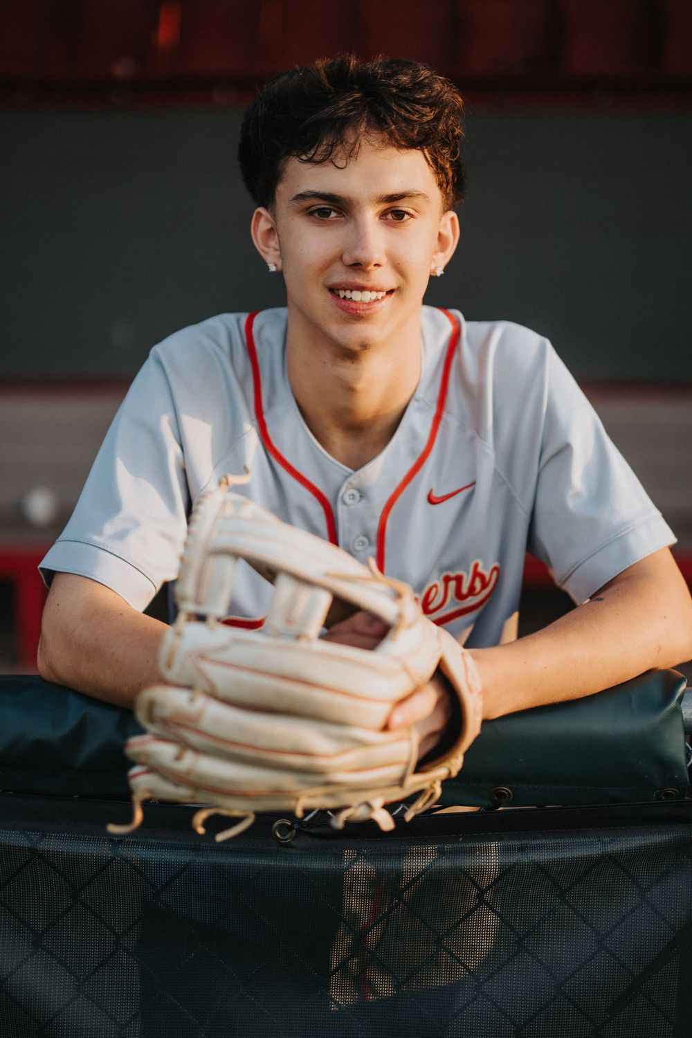 Baseball player leaning on fence with baseball glove in dugout.