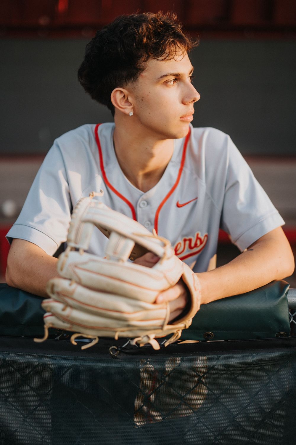Baseball player in white jersey leans against dugout railing with glove during game.