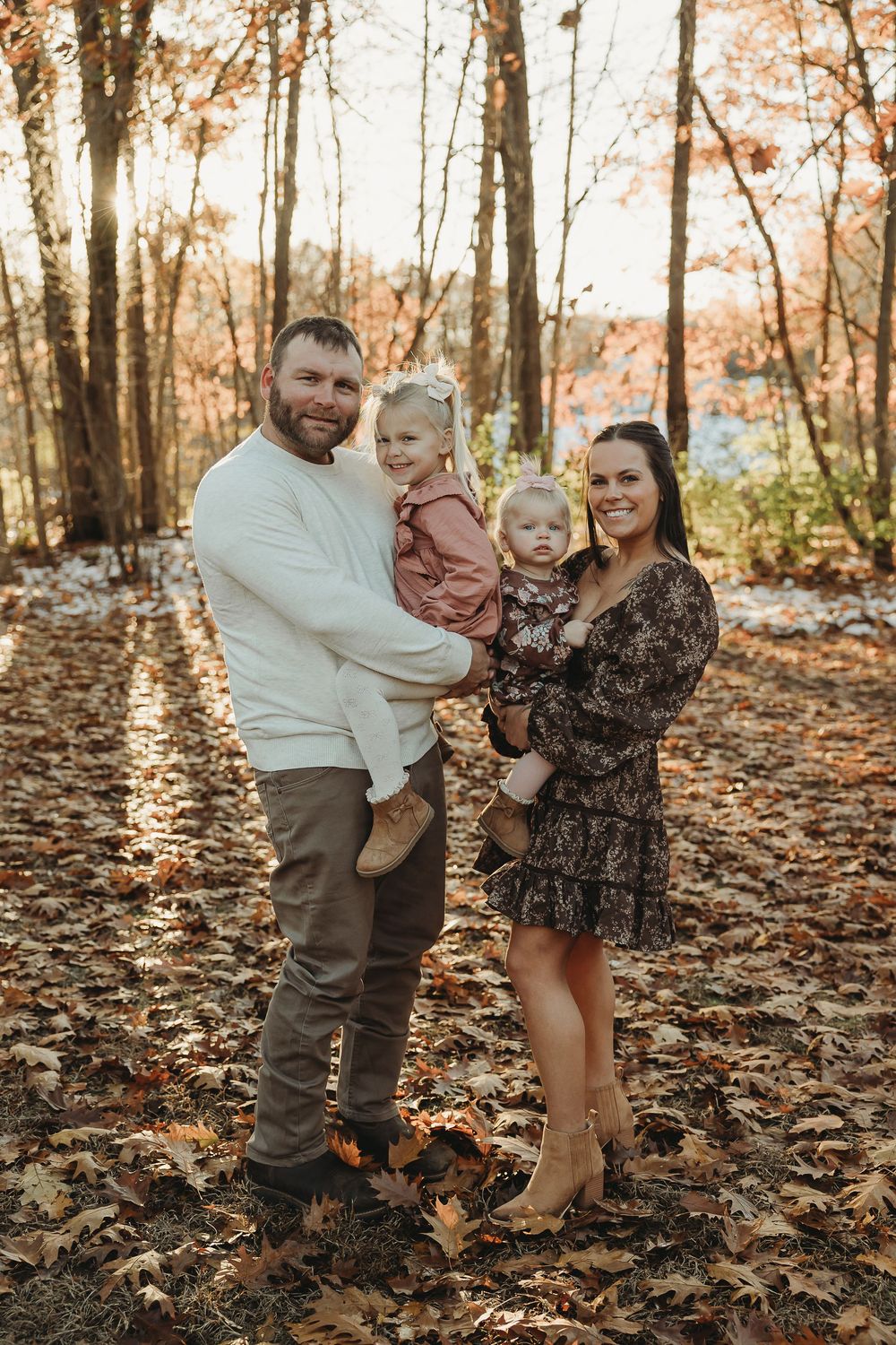 A family enjoys a playful autumn moment together in a forest covered with fallen leaves.
