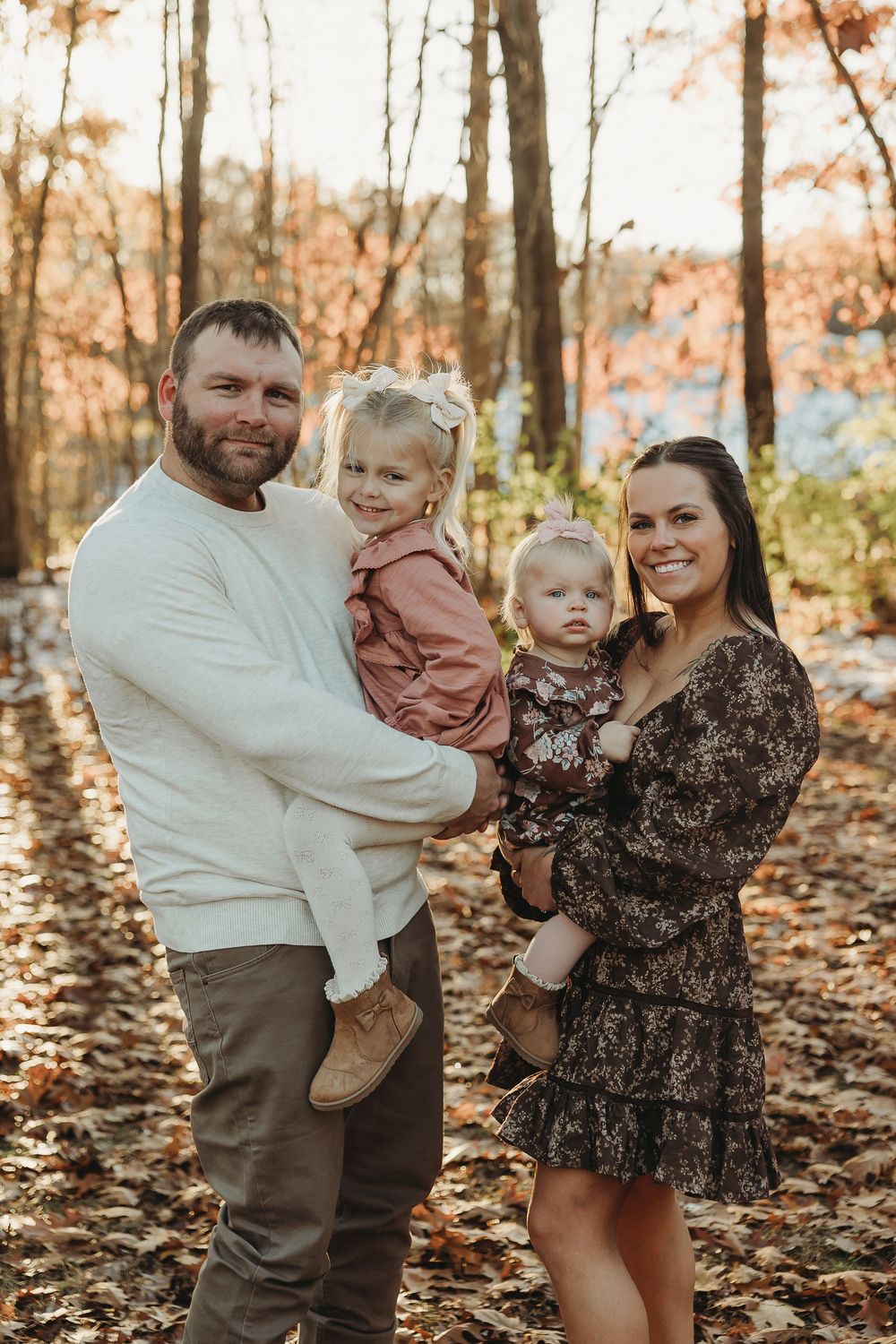 Family poses together in autumn forest with fallen leaves during golden hour sunset.