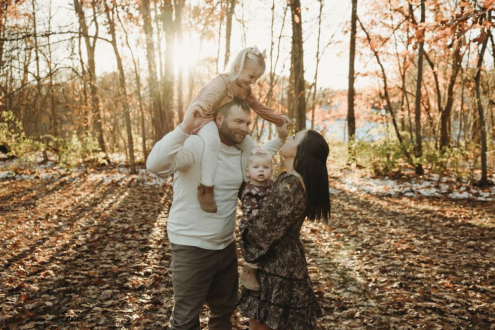 A couple shares tender moments together in a sunlit autumn forest during their engagement photo session.