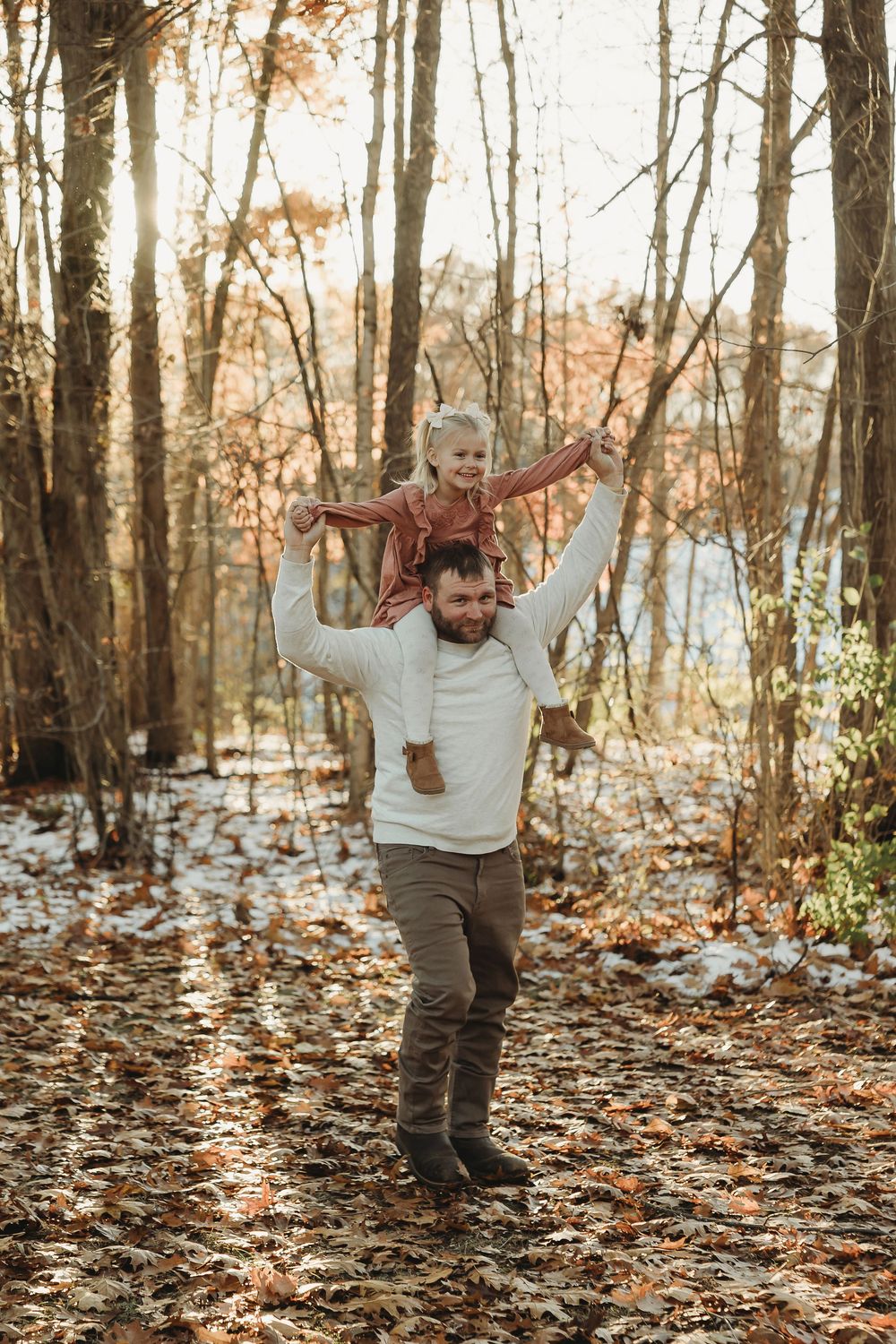 A child runs and plays joyfully through a forest filled with fallen autumn leaves on a sunny day.