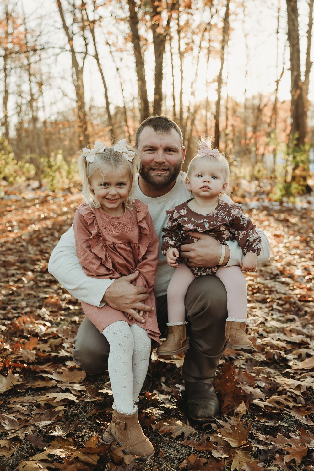 Family portrait in autumn forest with fallen leaves, wearing coordinated casual outfits in earth tones.