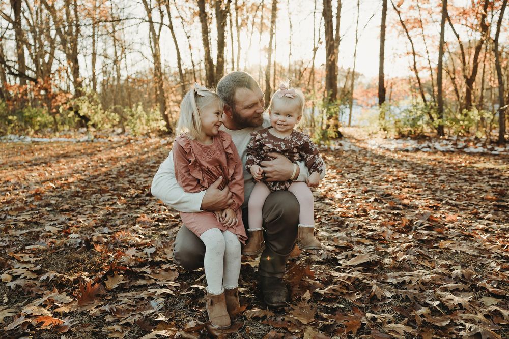 A couple sits together on fallen autumn leaves in a wooded area during a romantic outdoor photo session.