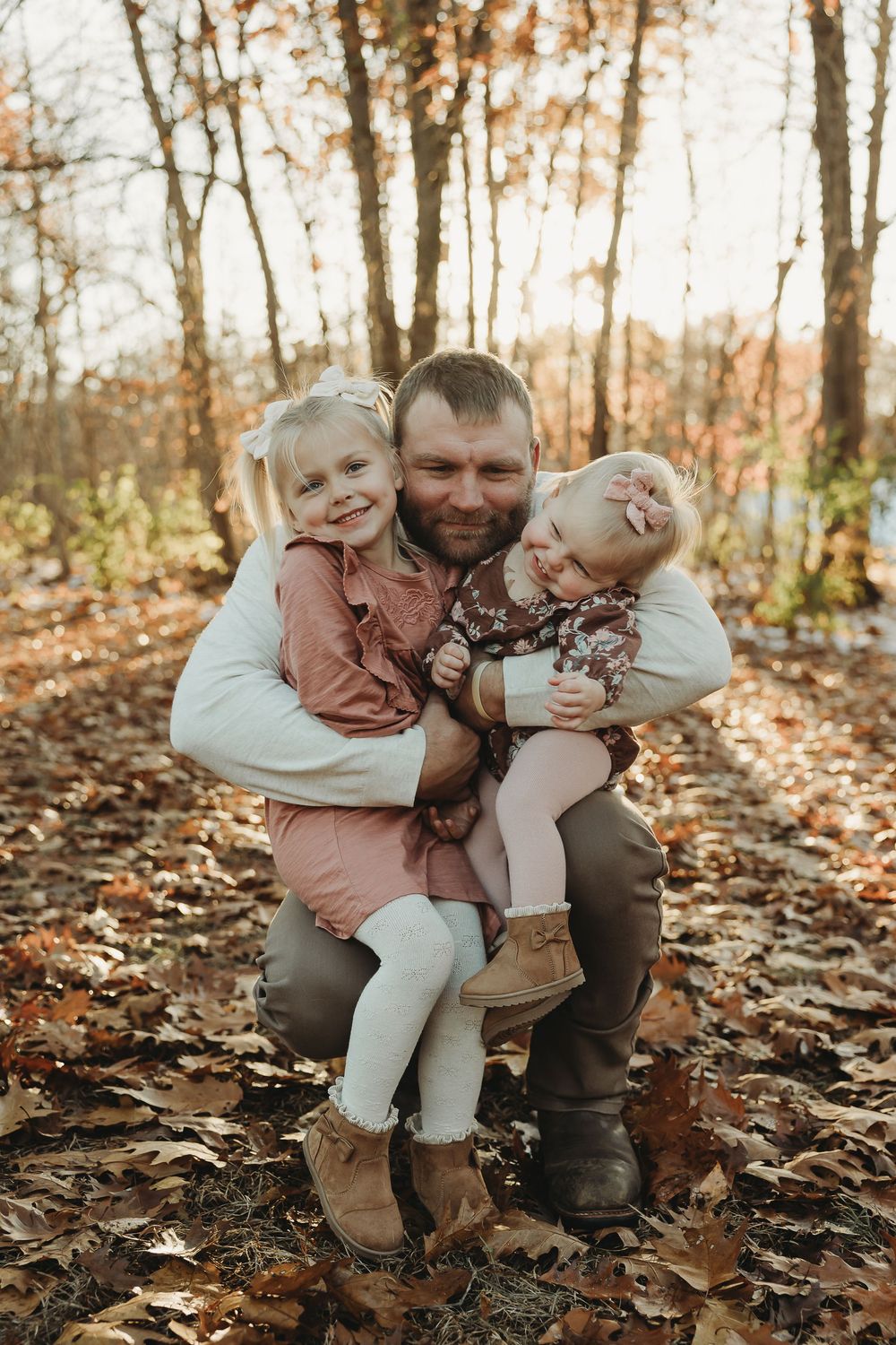 A loving family moment captured in autumn woods with fallen leaves and warm lighting.