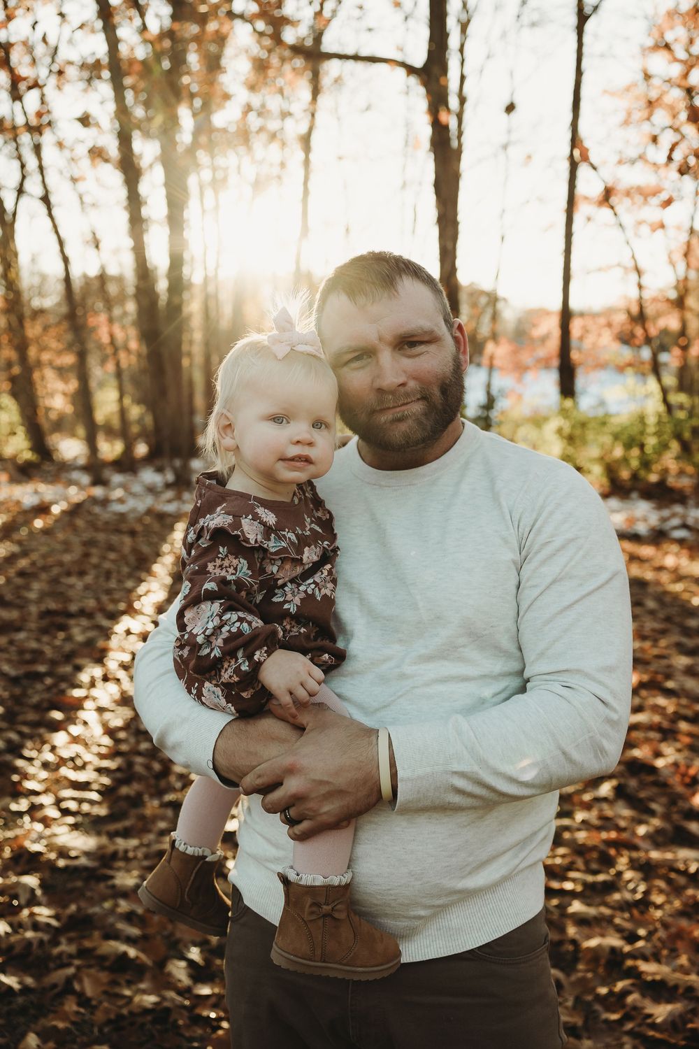 A parent and child share a tender moment in autumn woods with golden sunlight filtering through the trees.