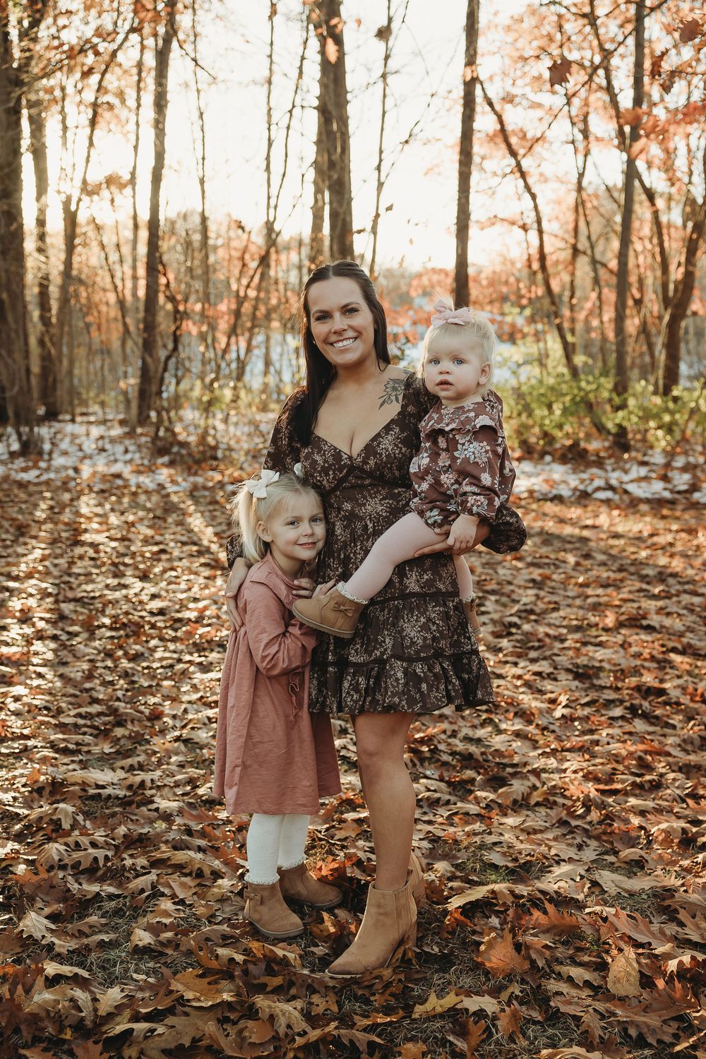Sweet family portrait session in a forest with autumn leaves scattered on the ground.