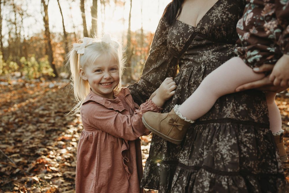 Candid family interactions during a fall photoshoot among scattered leaves in the woods.