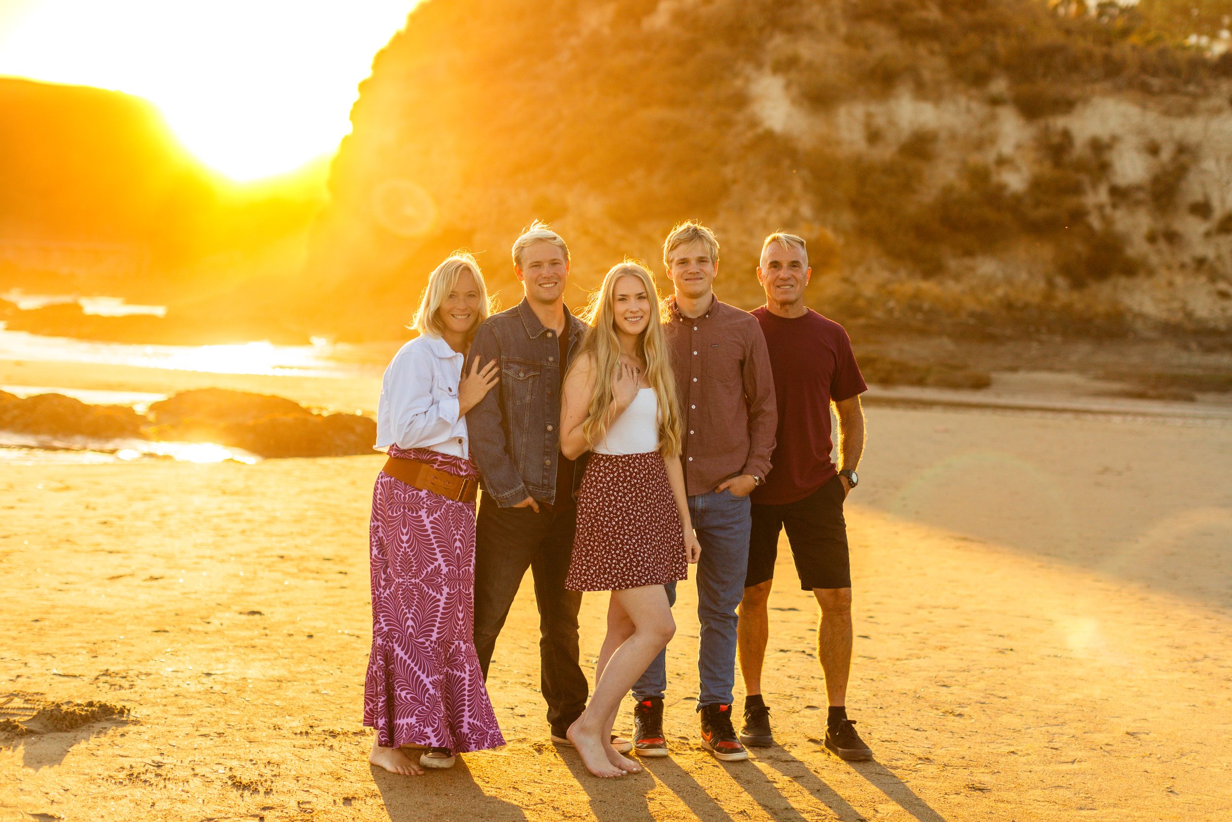 A group poses together on a beach with dramatic sunset lighting and cliffs in the background.