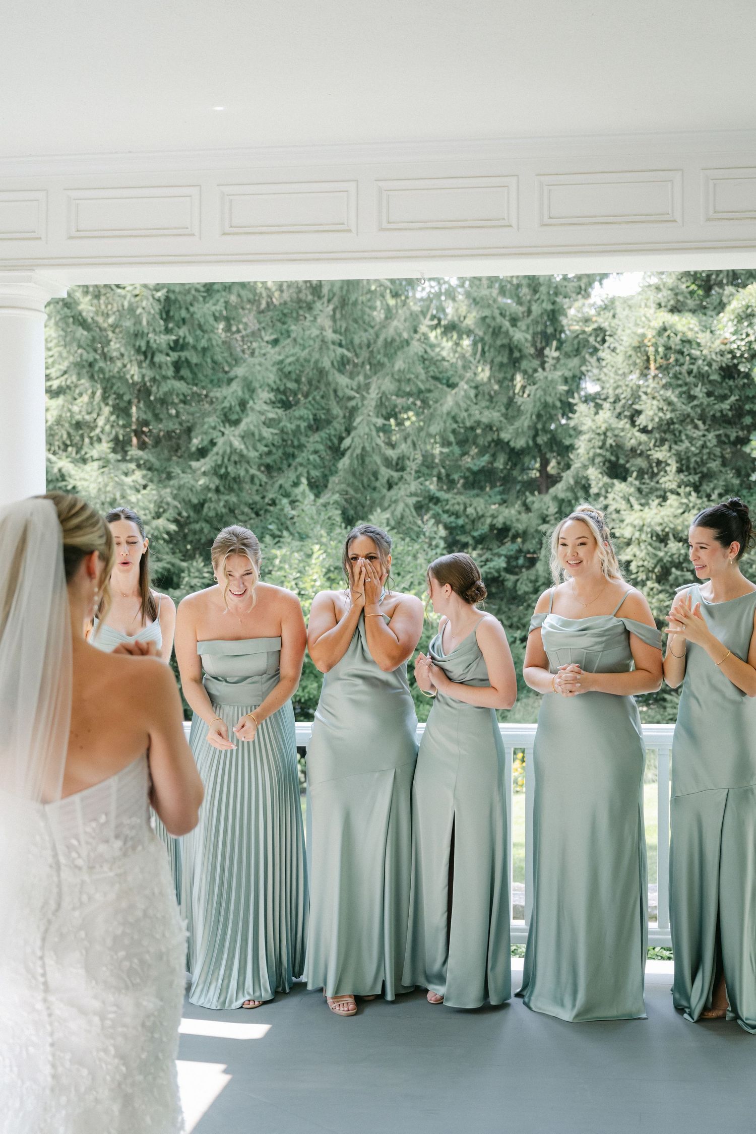 A group in matching sage green bridesmaid dresses stand together in a row during a wedding celebration. - Lake Forest
