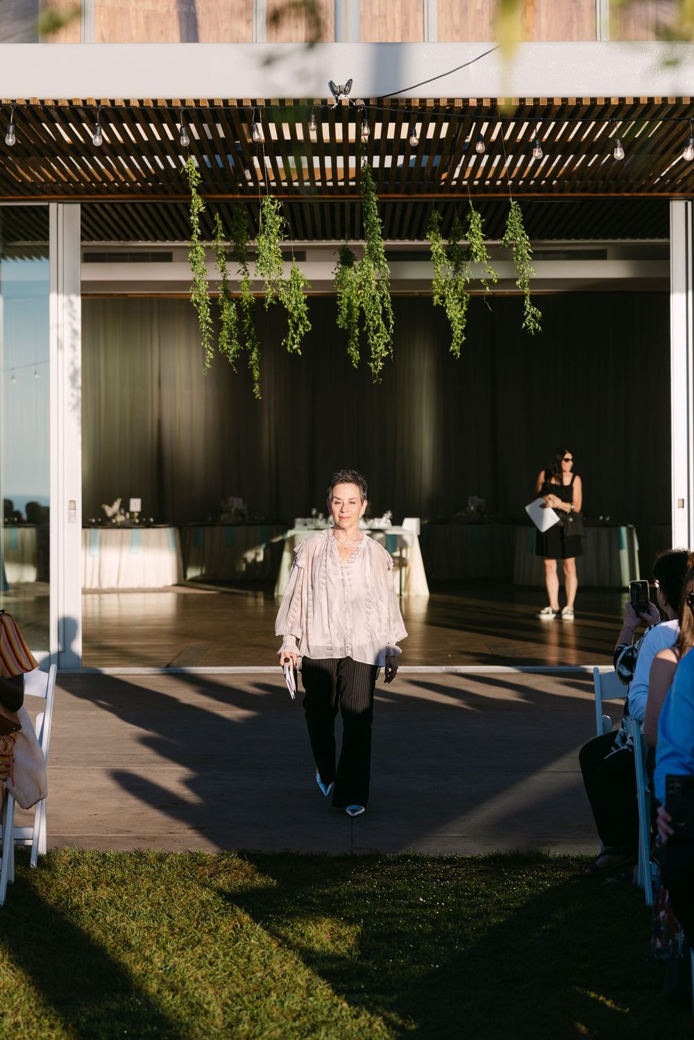 People dancing and enjoying themselves under a modern pergola structure with hanging greenery at an outdoor event.