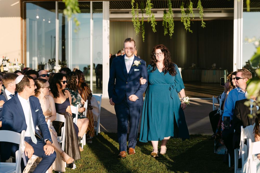 Wedding guests mingling during a cocktail hour in a contemporary indoor-outdoor space with hanging greenery.