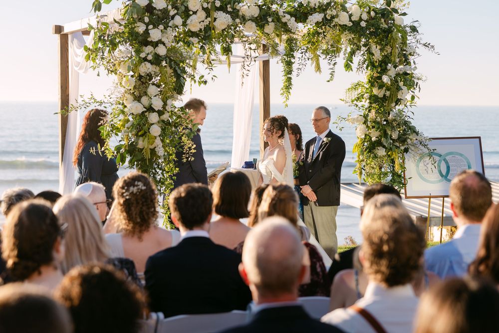 Wedding ceremony setup with white floral arch overlooking a scenic waterfront view.