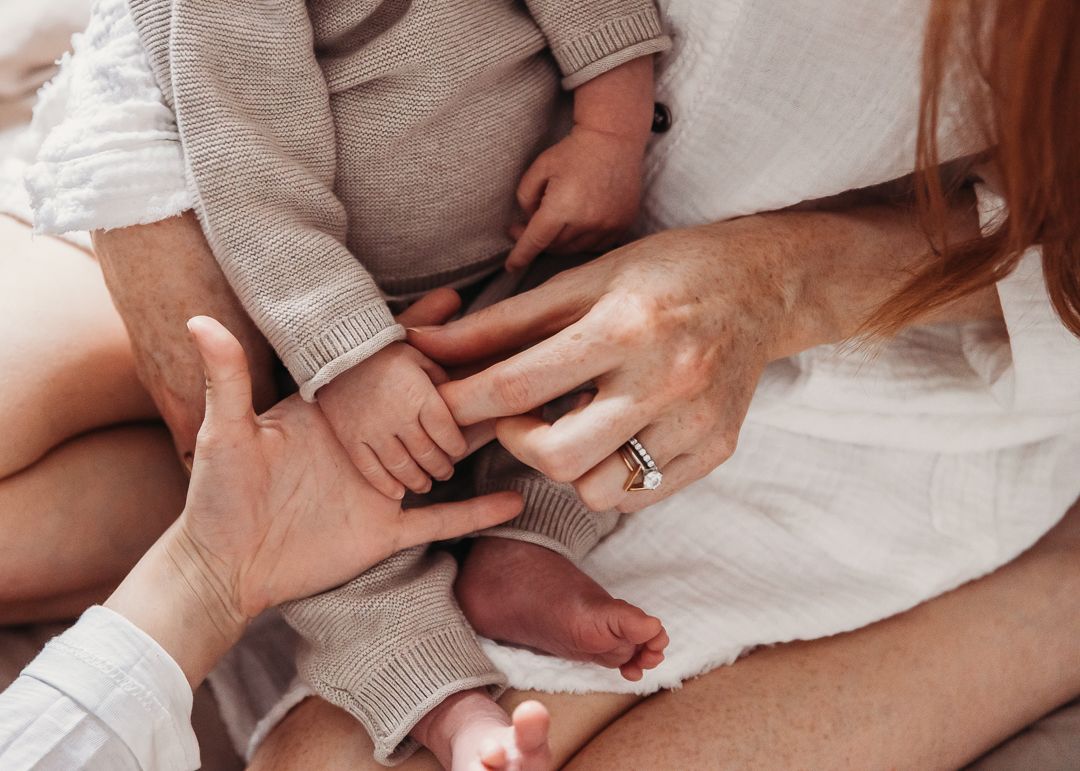 Small hands tenderly touching show a loving family moment on white textiles.