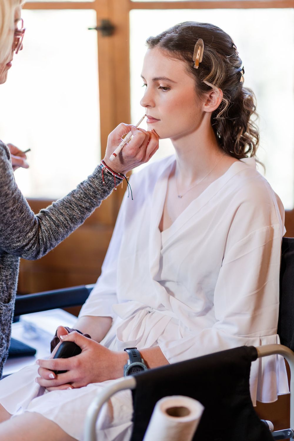 Wedding preparation scene showing makeup application in a bright room with natural lighting.