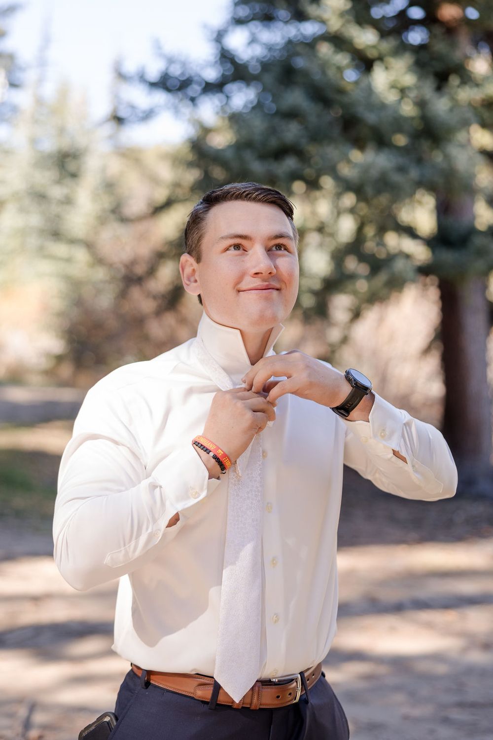 Someone in a white dress shirt adjusts their collar while posing outdoors.