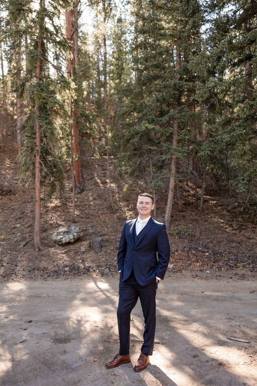 Person in navy suit poses in wooded outdoor setting with natural lighting.