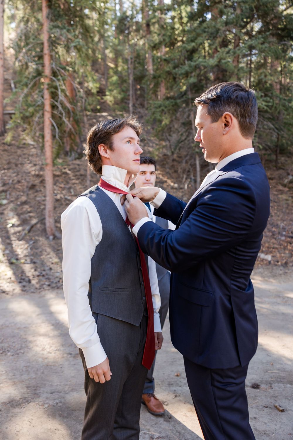 Two men in formal attire having a playful interaction outdoors in a wooded setting.