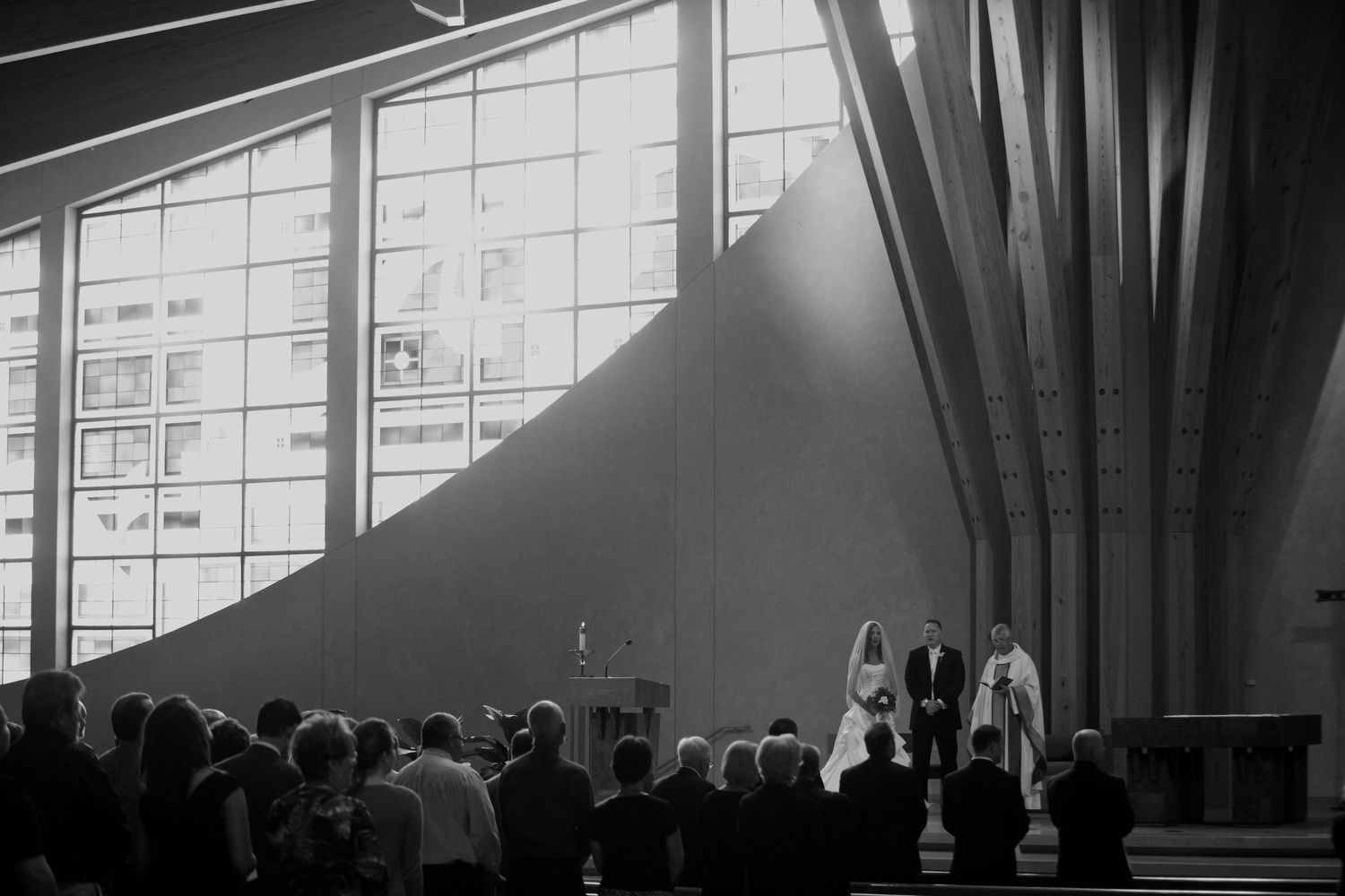 Black and white photograph of a dramatic architectural interior with curved beams and large windows casting shadows.