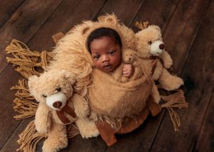 Newborn baby wrapped in brown fur surrounded by teddy bears in a lion-themed setup.