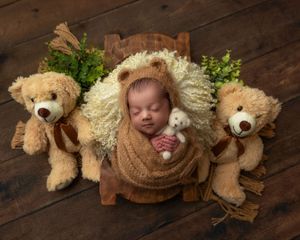 Newborn baby in bear ear bonnet sleeping between two teddy bears holding a small knit stuffed animal.