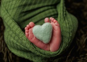 Close-up of newborn baby feet wrapped in green blanket holding a mint felt heart.