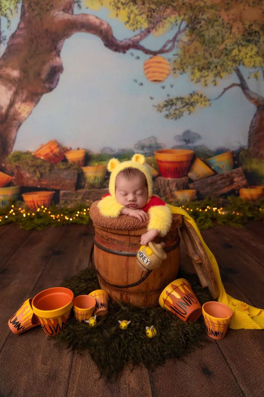 Newborn baby sleeping in a wooden honey barrel wearing Winnie the Pooh costume with yellow bear ears hat.