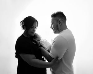 Black and white portrait of parents lovingly cradling their newborn baby together.