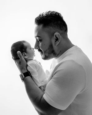 Black and white portrait of father holding newborn baby face to face.